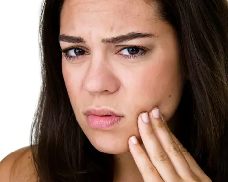 A person touches their cheek with a pained expression, suggesting discomfort or dental pain, against a plain white background.